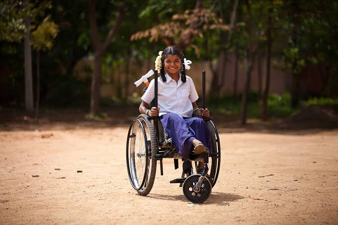 A young Dibyangjan girl in school uniform smiling in her wheelchair