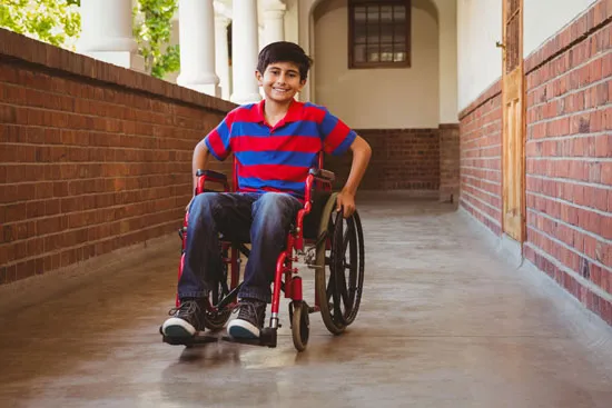 A young Dibyangjan student smiling in his wheelchair on a school campus